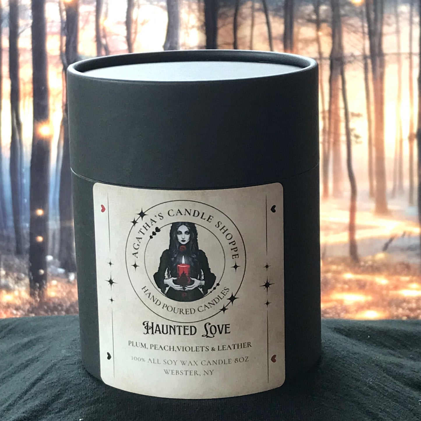 A gothic soy container candle with a label featuring a vintage love letter scene, set against a forest backdrop with lights.