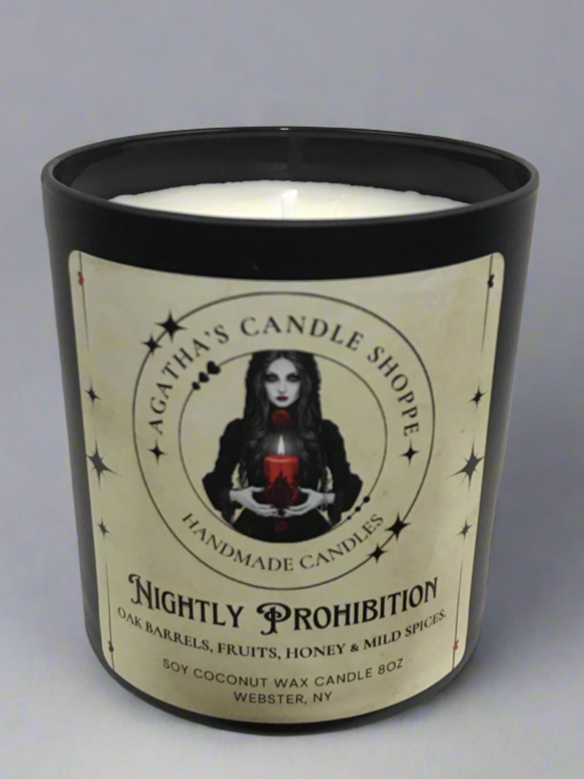 Candle box of 'Agatha's Candle Shoppe' label  as Nightly prohibition, scent of oak, fruit, honey and spice, with a gothic, witchy theme against a dim lit studio backdrop