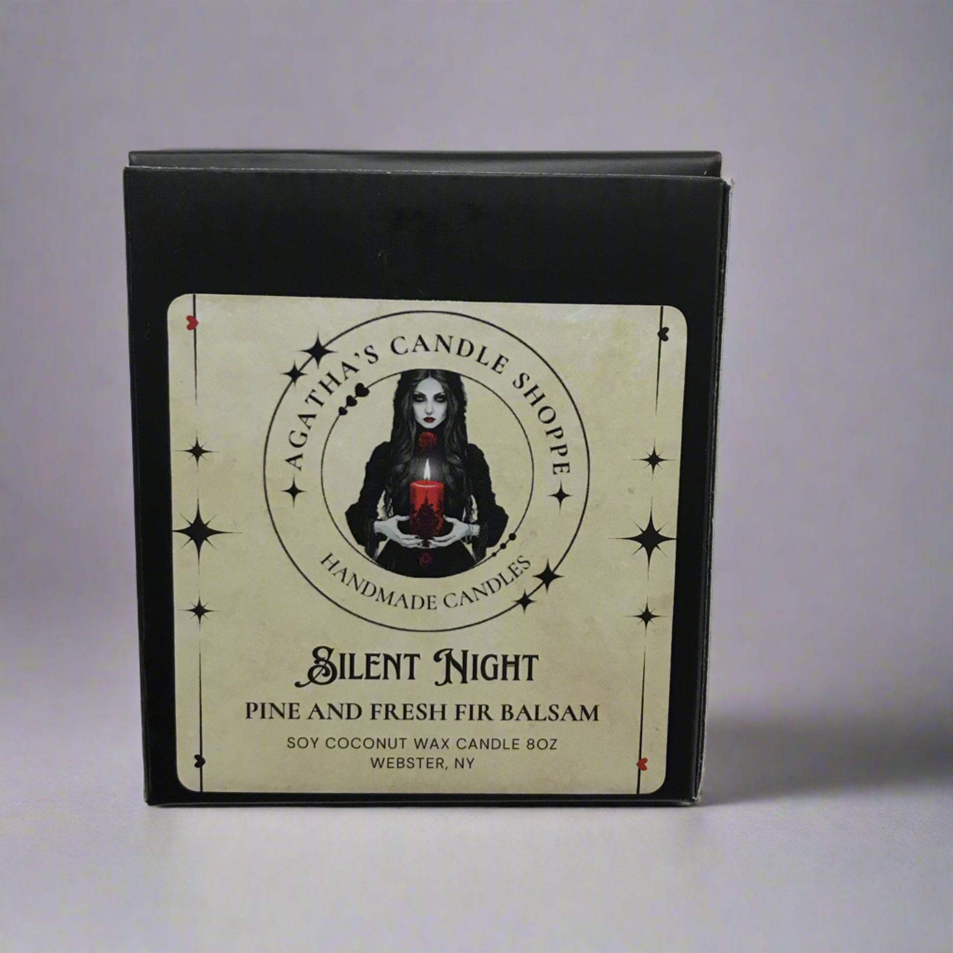 A black box of Agatha's Candle Shoppe's Silent Night soy and fresh fir balsam candle. The label features a woman with a red candle and star graphics.
